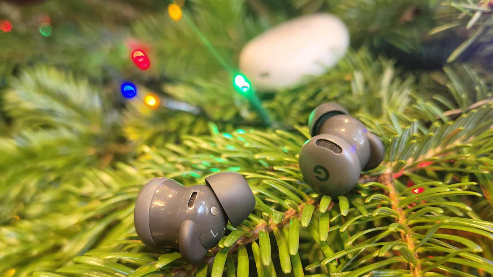The Google Pixel Buds 2a earbuds on a tree, with the case in the background.