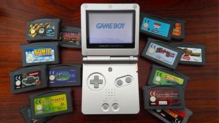 Game Boy Advance SP in silver surrounded by cartridges on woodgrain desk. 