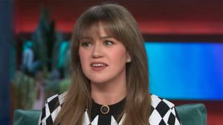 Kelly Clarkson looks very serious while talking with Cher in a checkered cardigan on her talk show. 