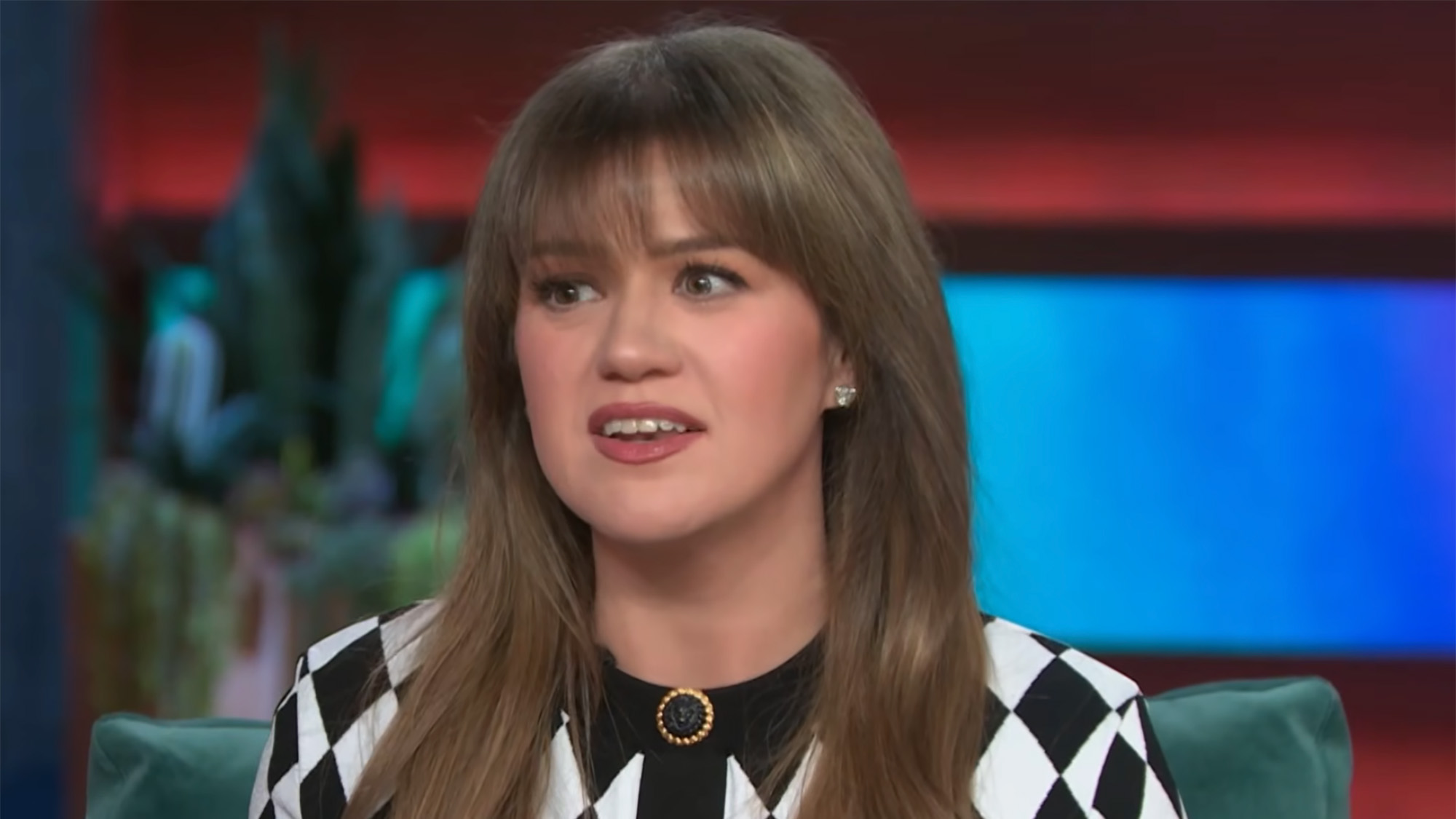 Kelly Clarkson looks very serious while talking with Cher in a checkered cardigan on her talk show. 