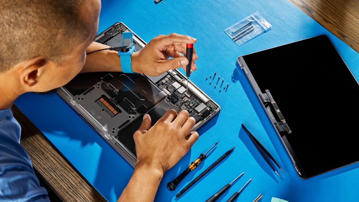 A person fixes a MacBook using one of Apple&#039;s Self Service Repair kits on a blue desk mat.