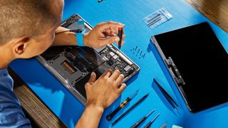 A person fixes a MacBook using one of Apple's Self Service Repair kits on a blue desk mat.