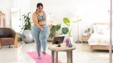 Woman exercising at home in front of a tablet on a coffee table