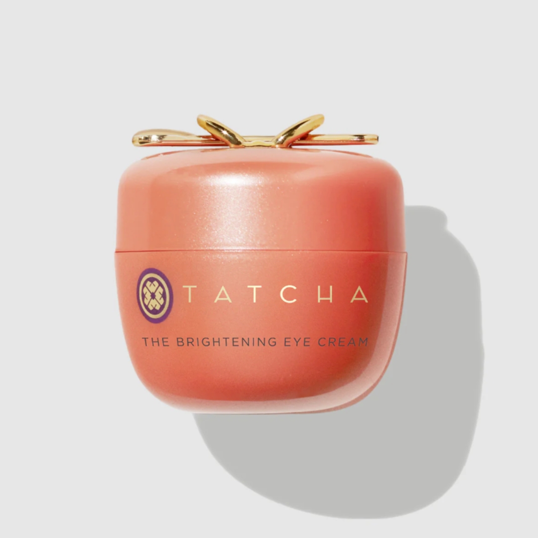 A product shot of the orange Tatcha Brightening Eye Cream, on a grey background