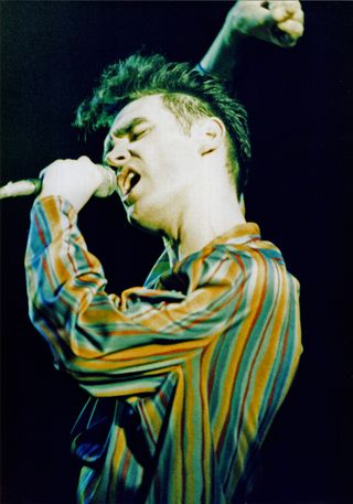 morissey wearing a colorful striped shirt performing on stage and dancing in the smiths