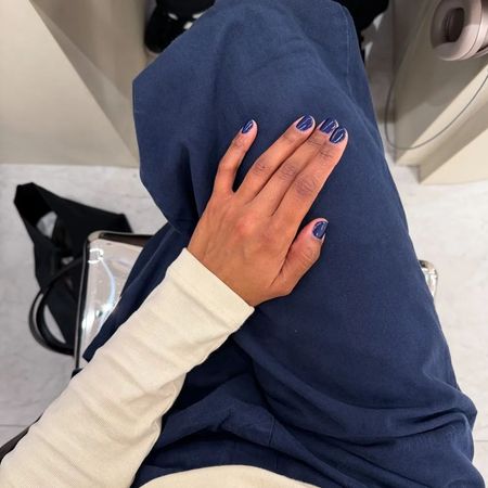 A woman taking a picture of her navy blue manicure, wearing matching blue trousers