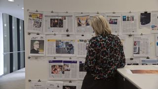 En bild från The Great Hack där en kvinna står och kollar på en vägg täckt av nyhetsartiklar.