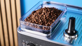 a black espresso machine by kitchenaid photographed against a blue background with silver chrome buttons and a pressure dial and steam wand