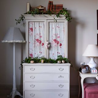 upcycled white painted dresser with floral fabric behind glass decorated for christmas