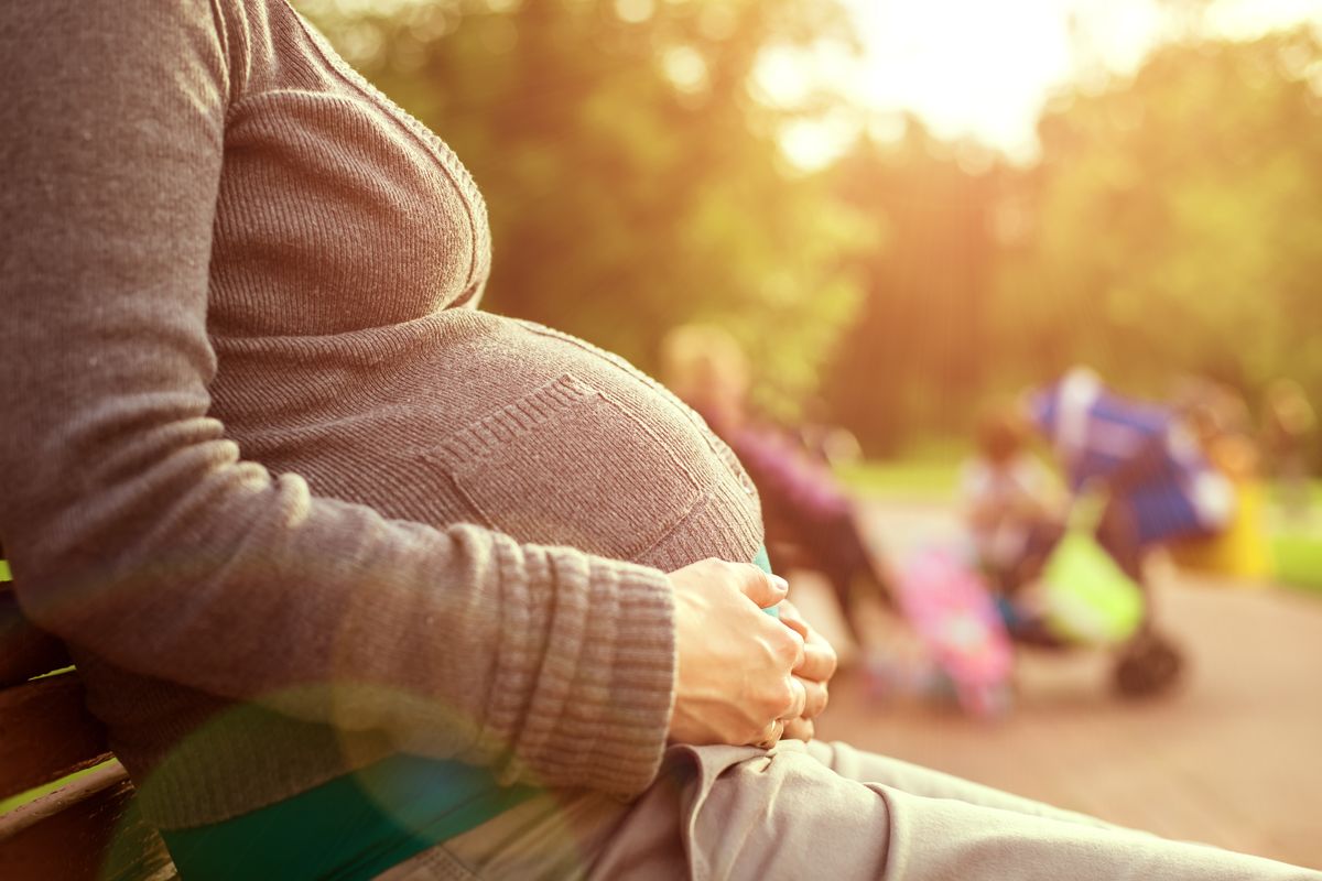 A pregnant woman sits out in the sun.