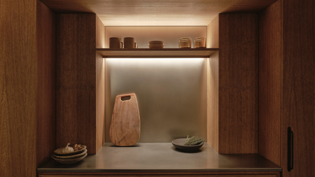 A kitchen in a Japanese home with a backlit shelf, a leaning cutting board, a bowl, and some glasses