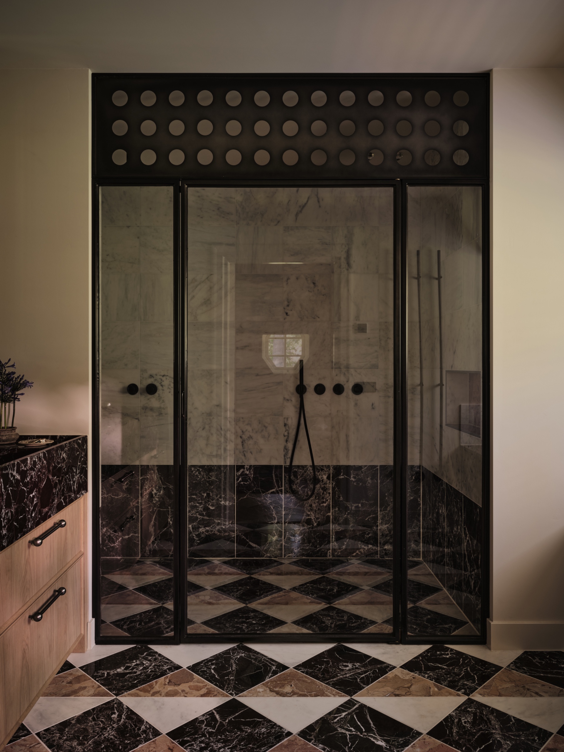 Bathroom with a black-framed glass shower enclosure, geometric black, white and pink marble flooring continuing into the shower, and a wood vanity.