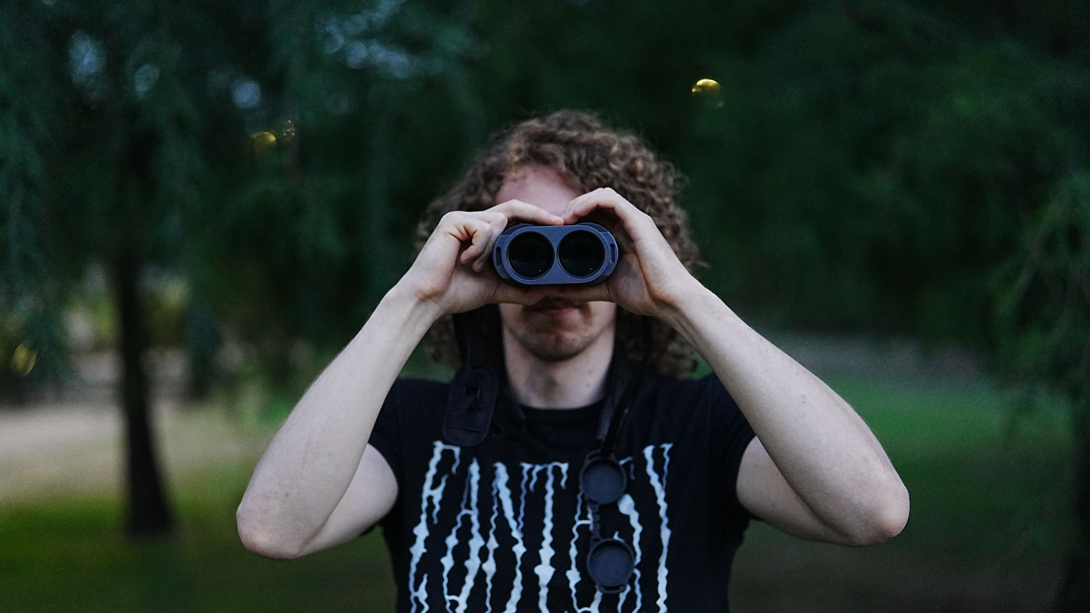 A head-on view of a man looking through the Fujifilm Techno-Stabi TS-L 1640 image-stabilized binoculars with trees in the background.