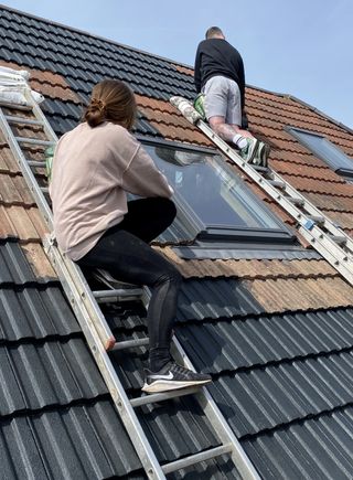 The couples on ladders painting the roof tiles black individually