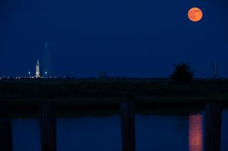 The supermoon full moon of July 12, 2014 rises into the night sky above NASA's Wallops Flight Facility in Wallops Island, Virginia, where a private Antares rocket (left) built by Orbital Sciences Corporation stands poised for a July 13 launch.