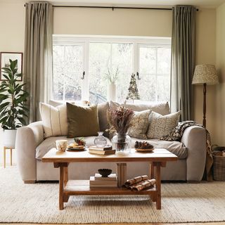 A living room in a neutral, earthy colour scheme with a beige sofa, cream rug and olive green semi-sheer curtains