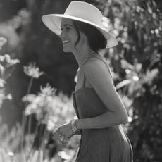 Meghan Markle wearing a sleeveless dress and sun hat smiling and turning to the side