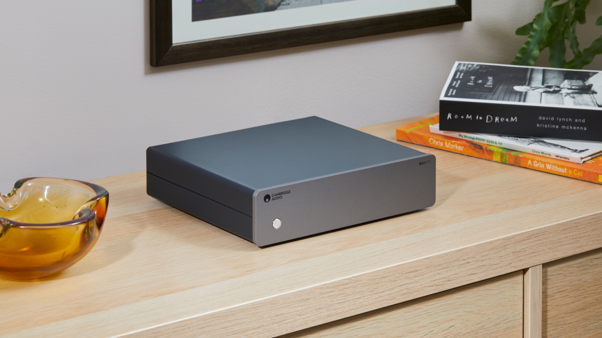 Cambridge Audio MXW70 amplifier on a wooden sideboard in a brightly lit room between an amber glass bowl and a small stack of books