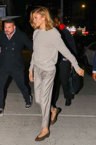 Zendaya wears a gray sweater with gray trousers and green flats.