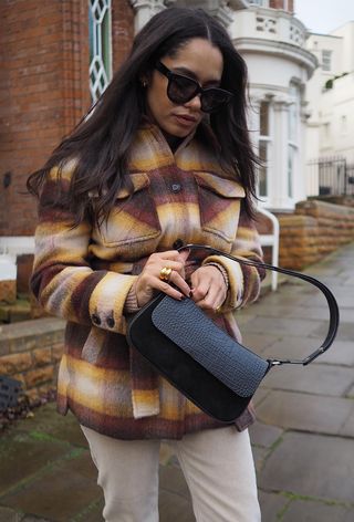 best womens shackets shown on a woman walking down a sidewalk wearing black sunglasses, a plaid jacket, tan skinny jeans, and a black shoulder bag