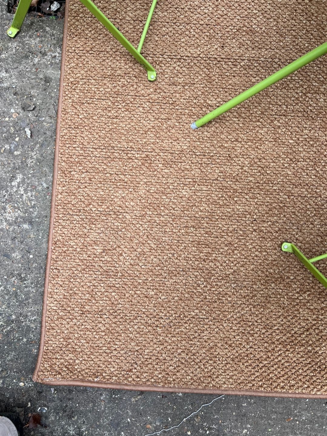 Close-up of a jute-inspired outdoor rug on a stone patio floor. The legs of lime green outdoor furniture are in view.