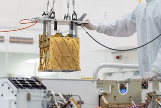 a golden metal cube is being lifted by a person in a white clean suit in a laboratory