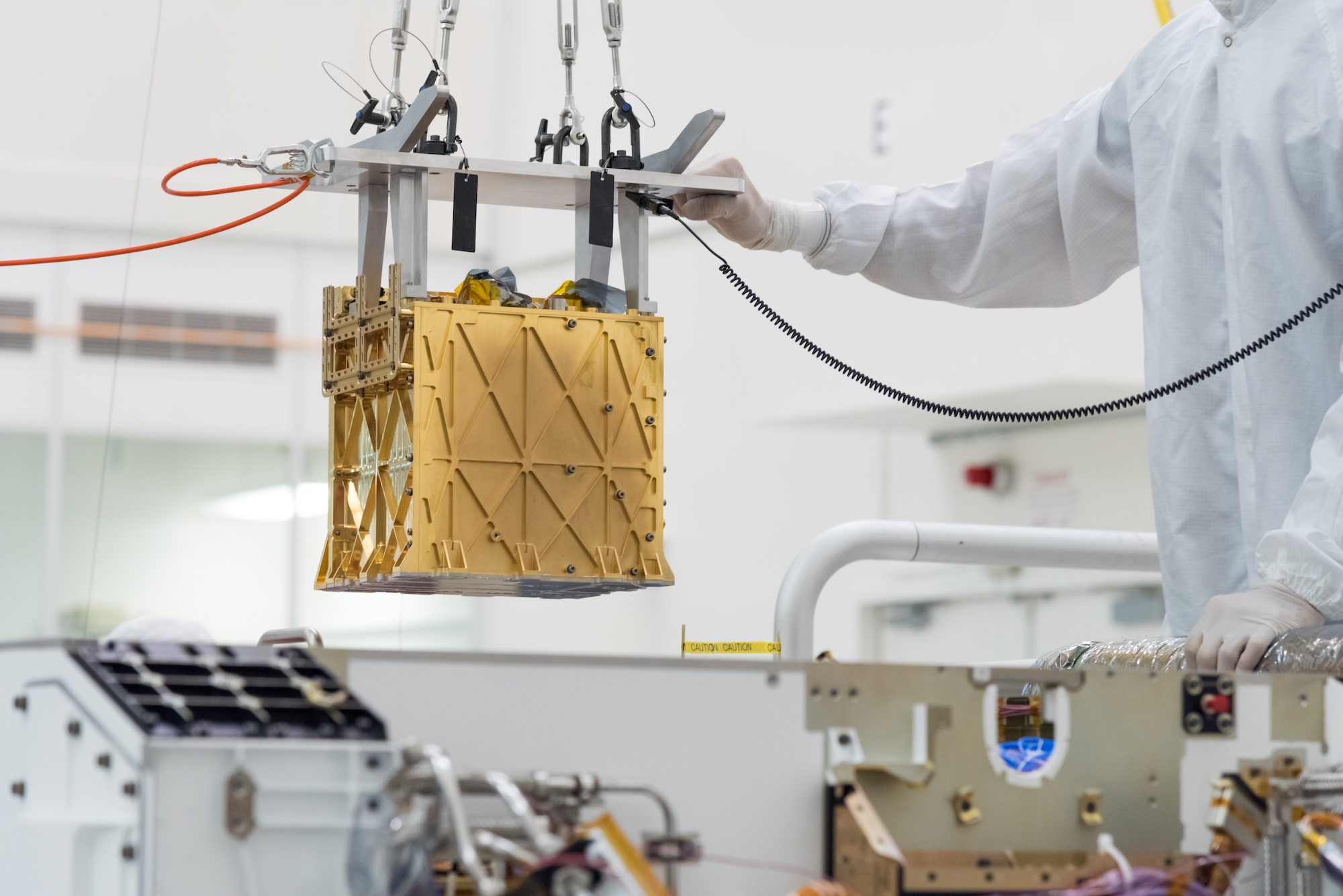 A golden metal cube is lifted by a person in a clean white suit in a laboratory