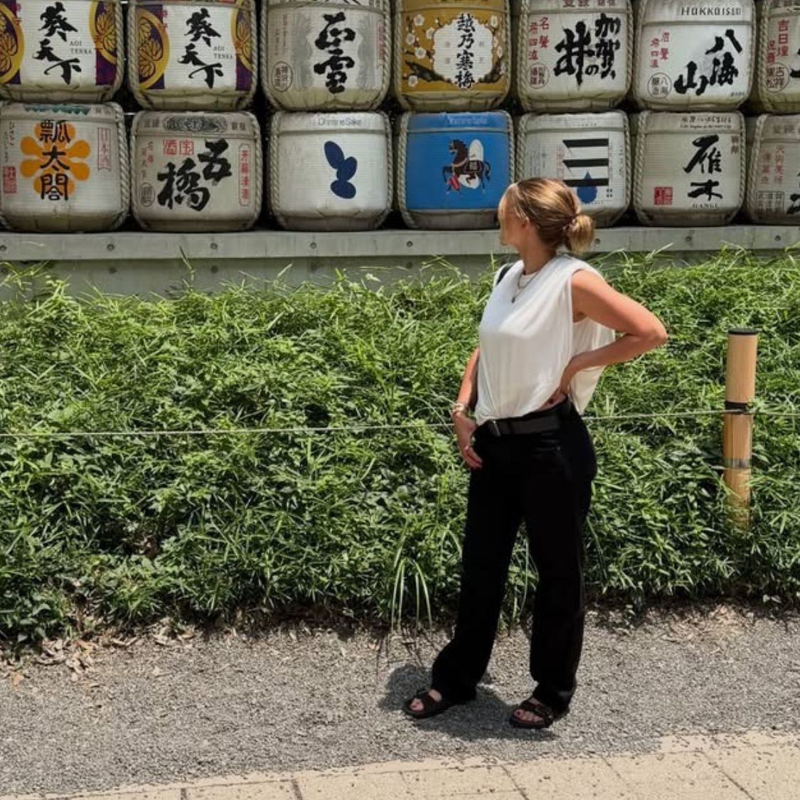 Sofia Richie Grainge poses for a photo wearing black trousers with black chunky sandals and a white top.