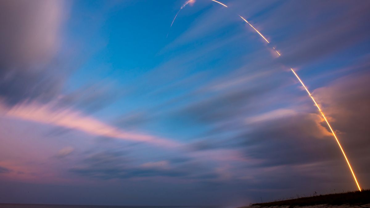 a rocket carves an arc of orange flame into a dusky sky.