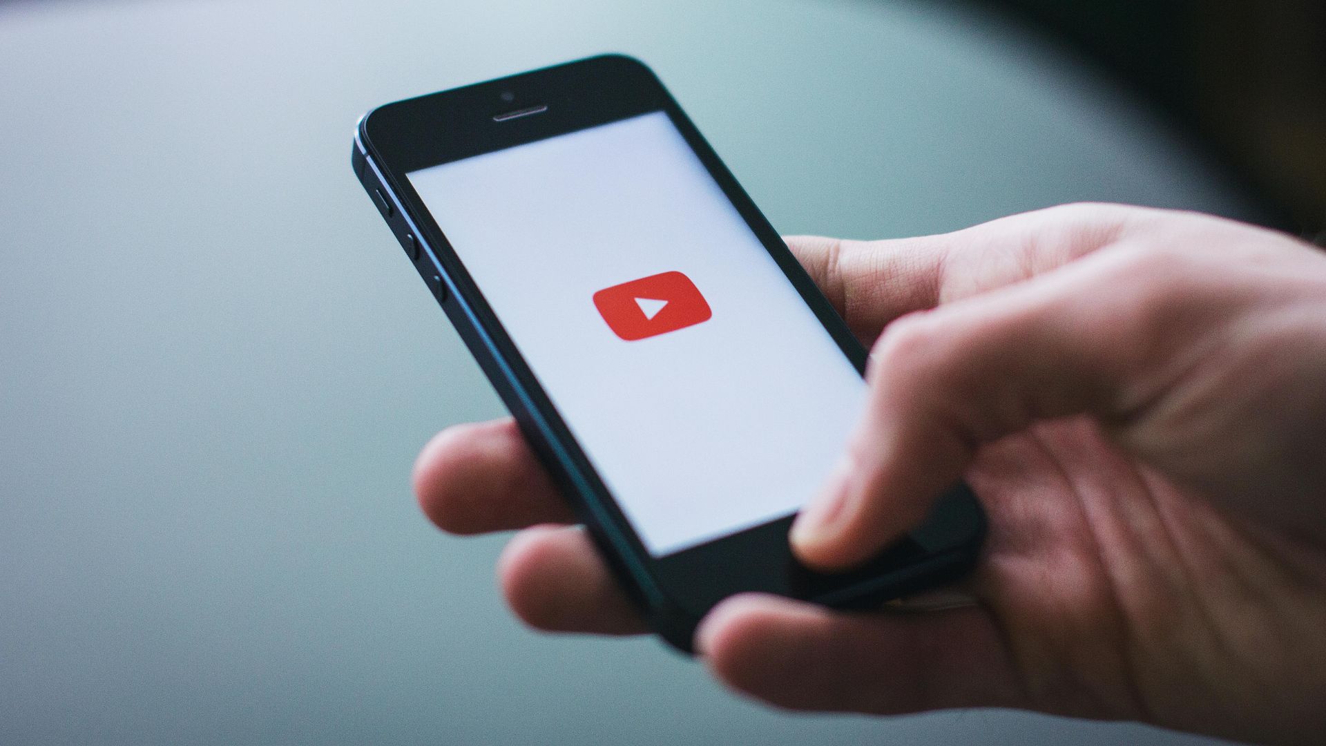 A hand opens the YouTube app on their iPhone