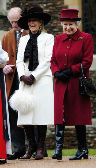 Duchess Sophie wearing a white coat and feather purse laughing standing next to Queen Elizabeth wearing a red coat and black boots