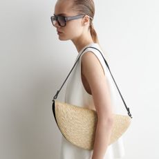 Woman wears a white top and carries a straw bag