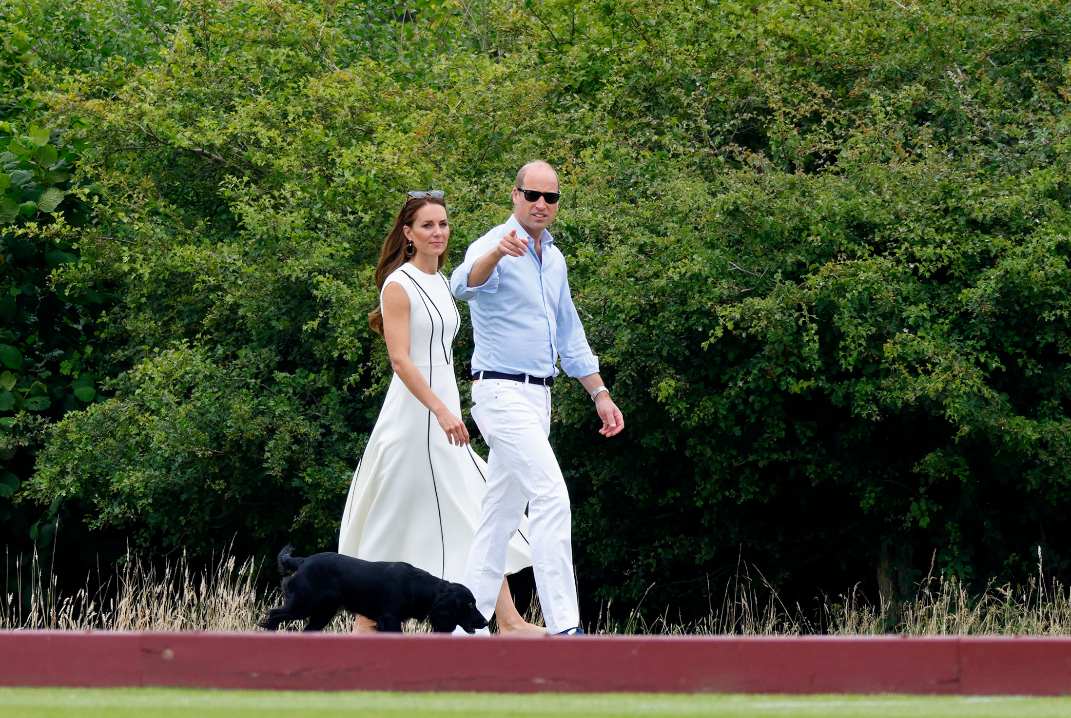 A man and woman walking outdoors beside a black Cocker spaniel.