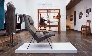 Reclining chair with grey upholstery, with the wooden loom in the background