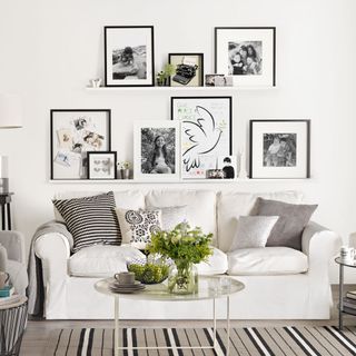 living room with white wall with multiple pictures and white sofa with multi coloured cushions