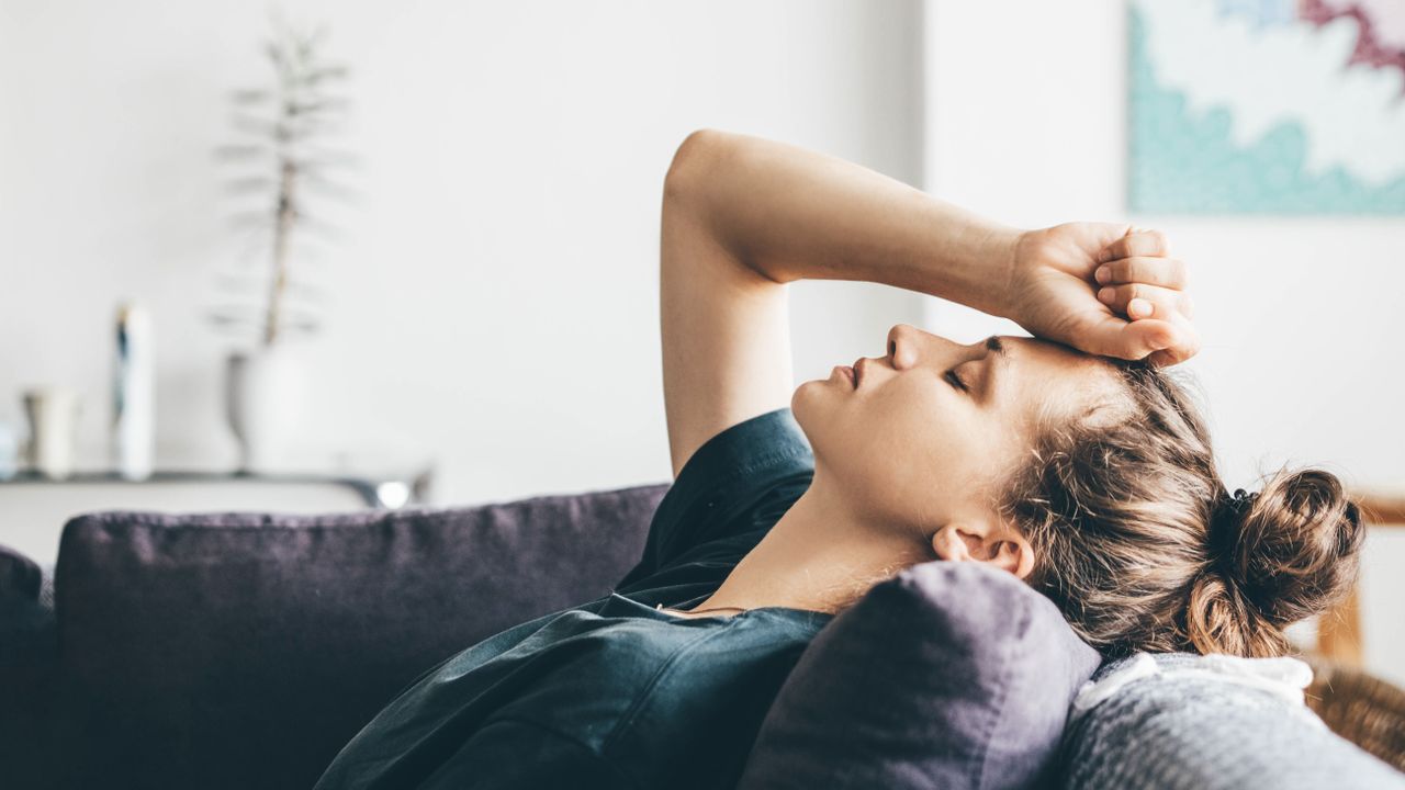 A woman reclining on a sofa with her hand clenched in a fist above her head and her eyes closed