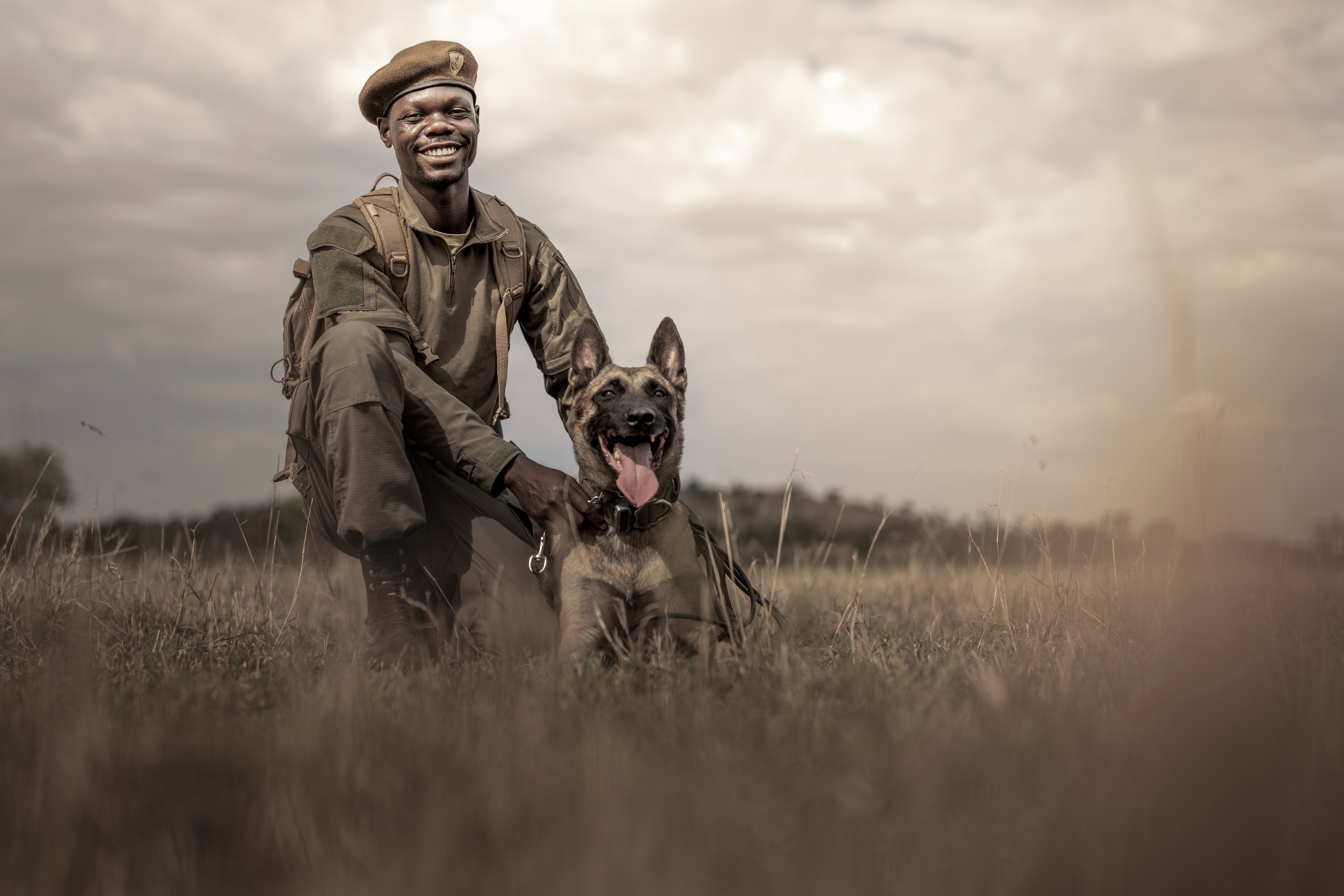 A man kneeling next to an anti-poaching dog in long grass