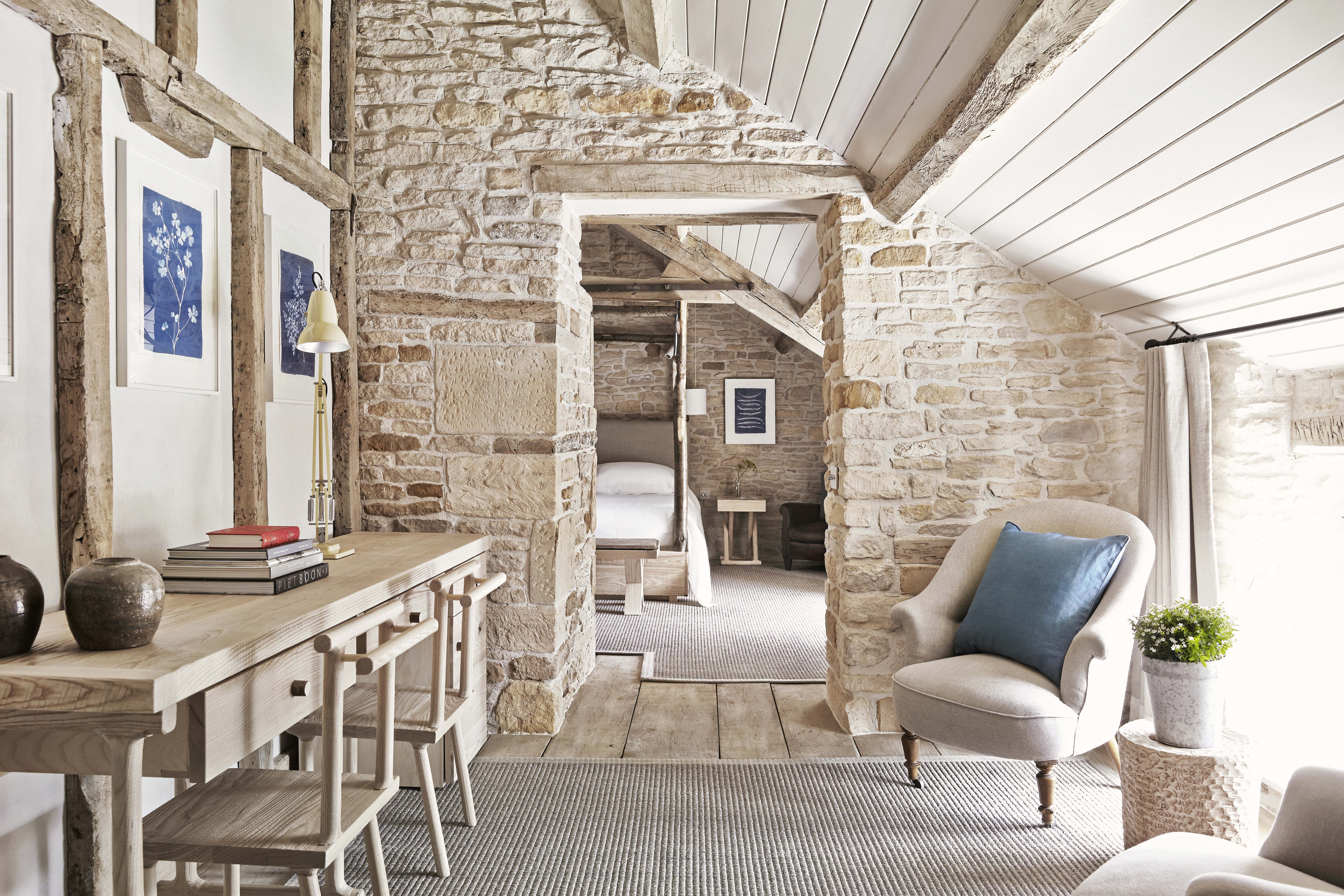 A hotel bedroom with bare brick walls, exposed beams and light wood furniture
