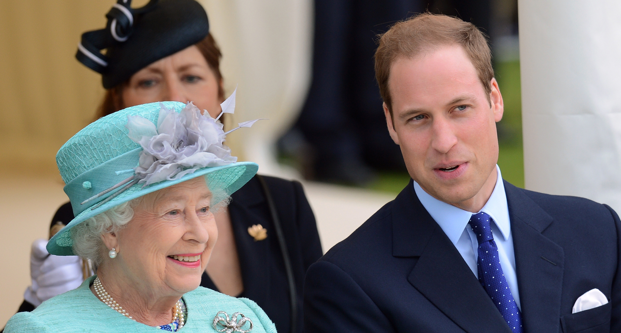Queen Elizabeth in a turquoise coat sitting next to Prince William