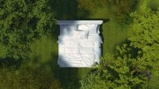 An organic mattress made up with white sheets in the middle of a green forest