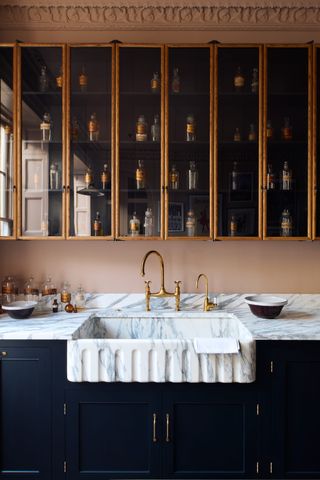 A kitchen with glass cabinets and marble sink with gold detailing