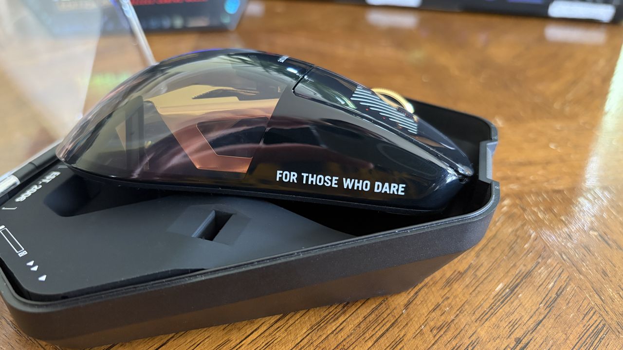 A glossy black ASUS ROG computer mouse with "FOR THOSE WHO DARE" printed on the side, sitting in a case.