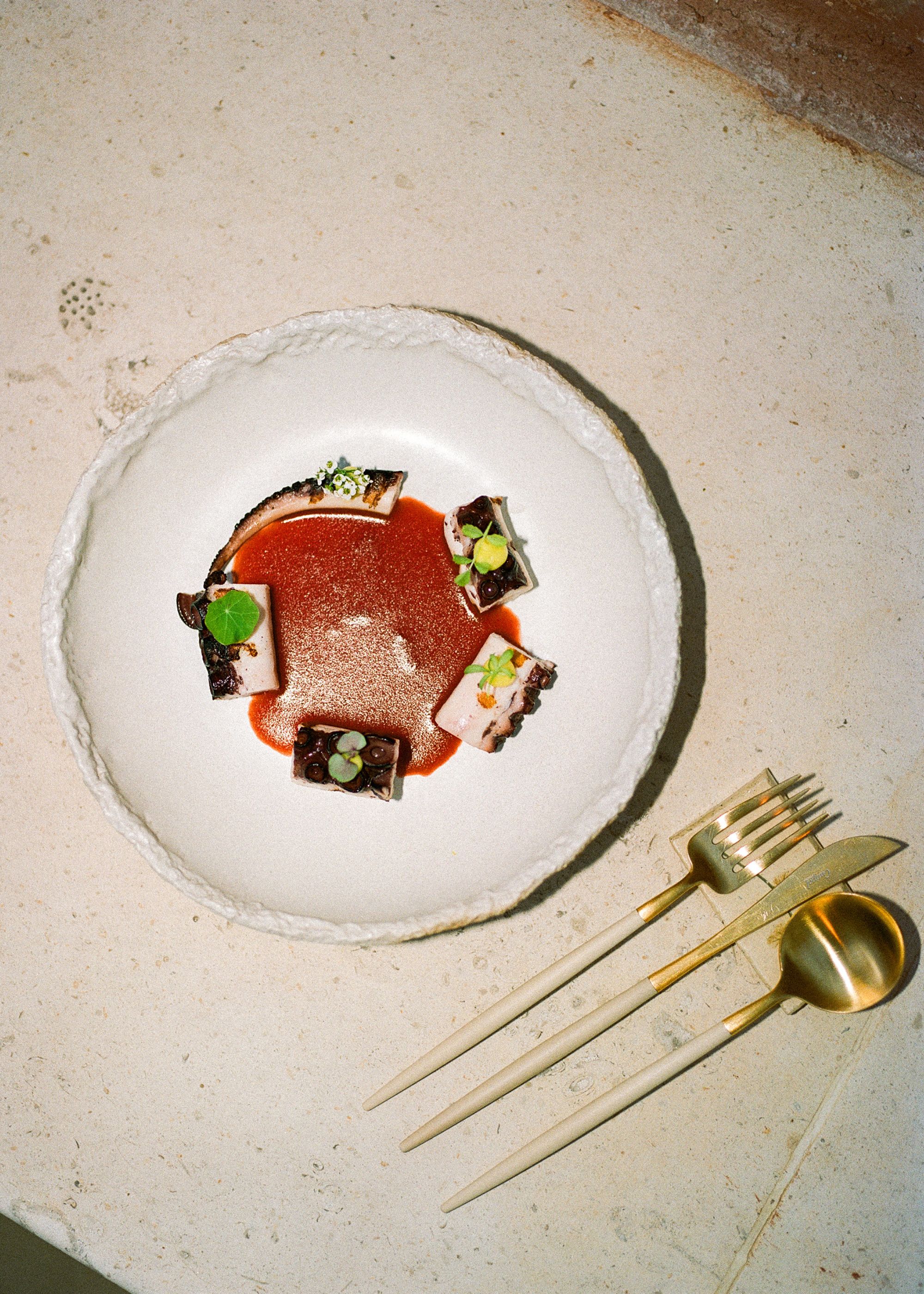 A plate of octopus and sauce, as well as golden cutlery 