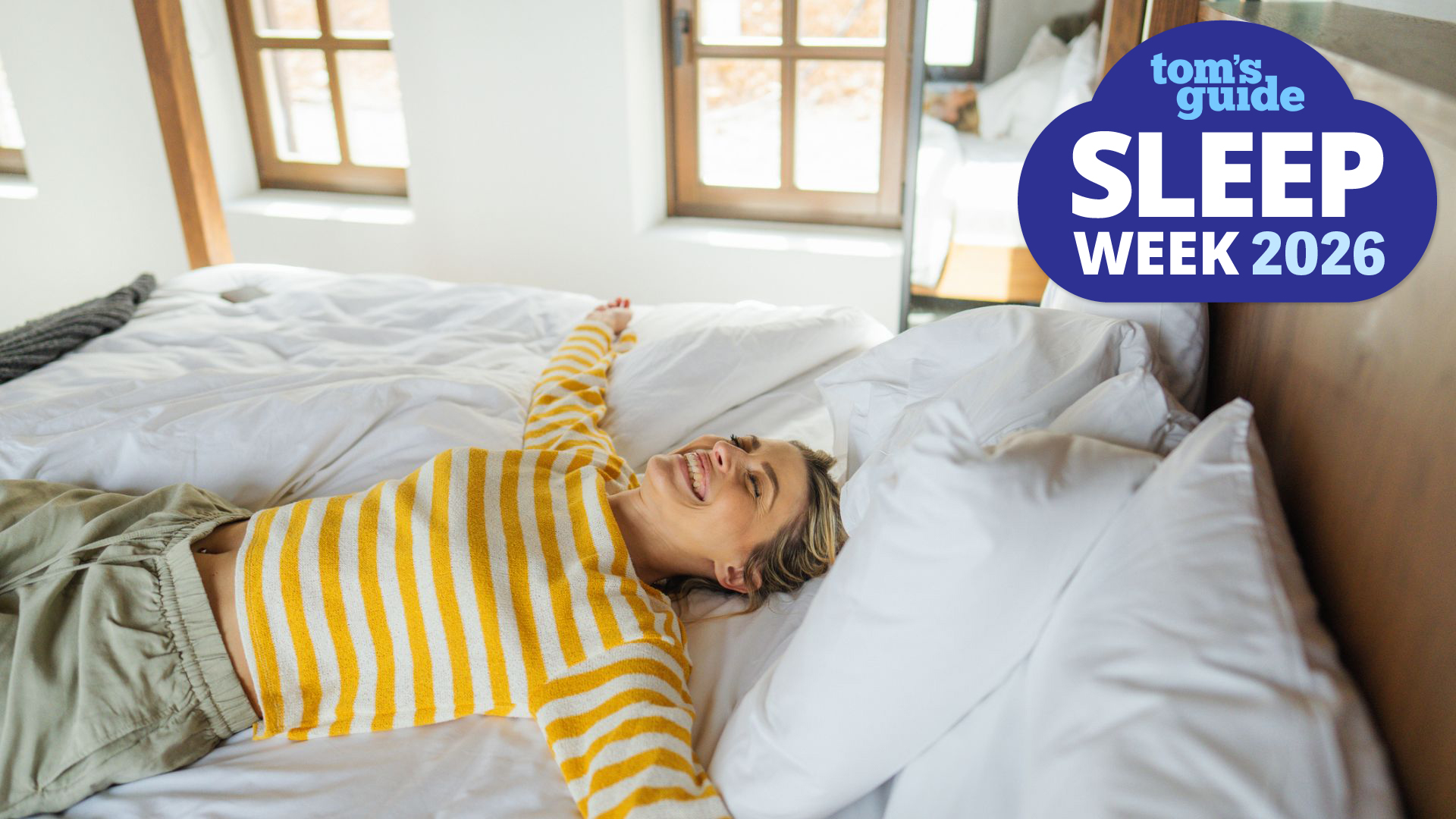 A woman lies on her back on her mattress on a sunny spring day, with a big smile on her face. In the top right corner is a Tom's GUide Sleep Week 2026 graphic