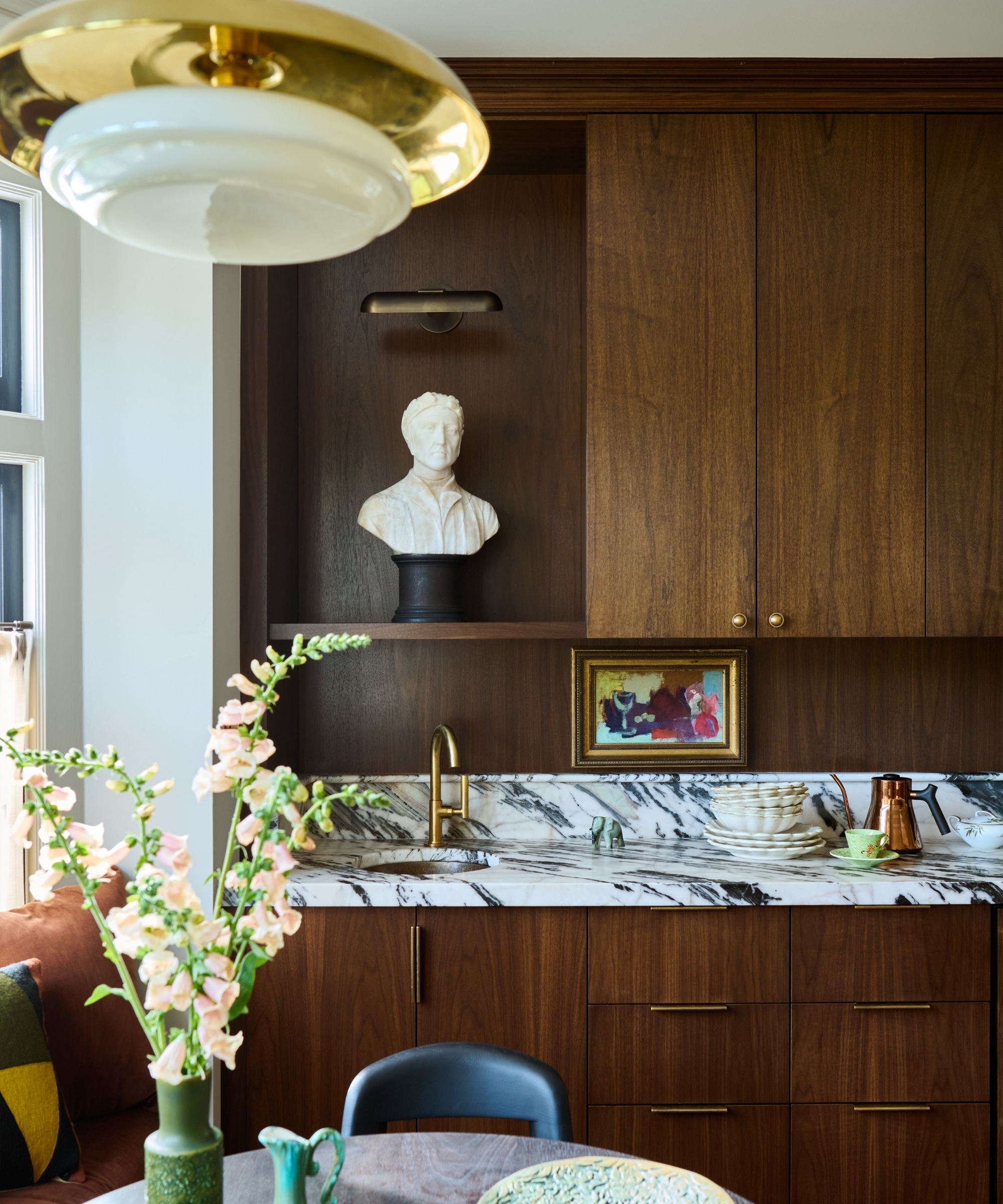 The corner of a kitchen with dark wood cabinets, marble countertops, and collected decor