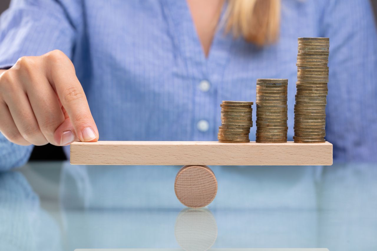 Woman sitting in front of small wooden seesaw with coins on it