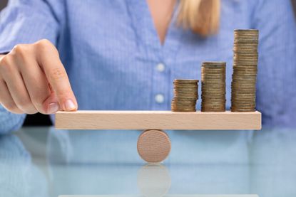 Woman sitting in front of small wooden seesaw with coins on it