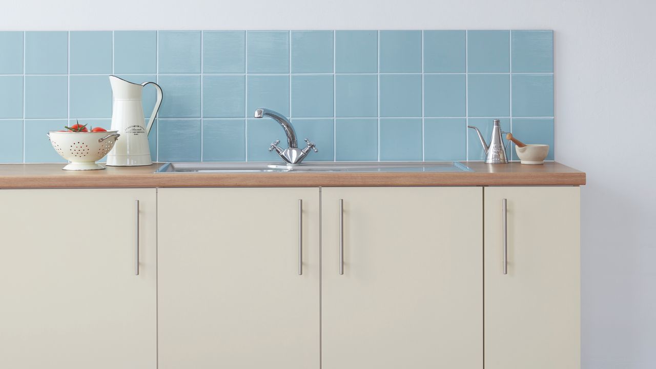 Blue wall tiles with white grout on top of white kitchen cupboards with sink