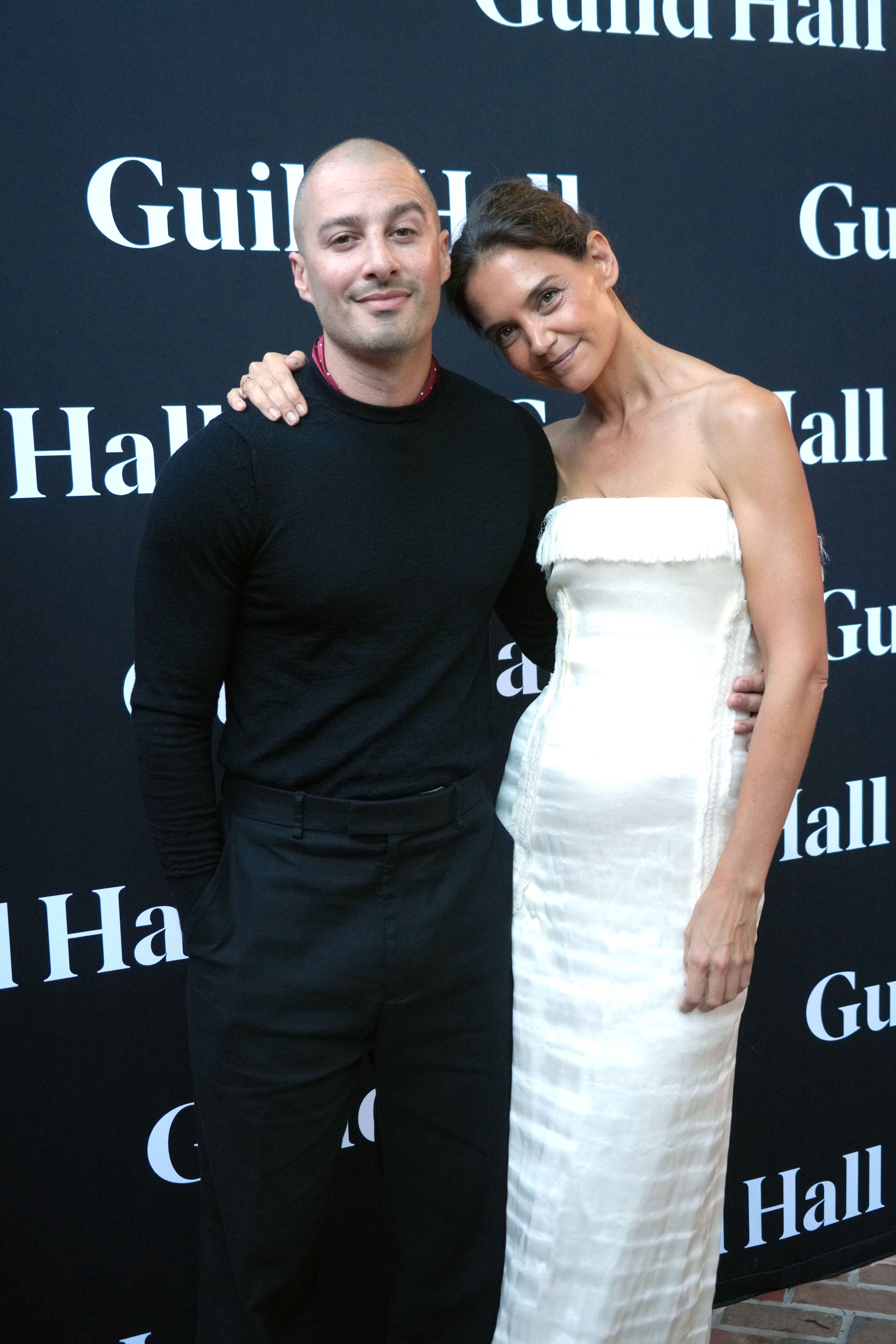 Katie Holmes wears a strapless white dress and carries a soft leather bag while posing with boyfriend Jason Bard Yarmosky at the 2026 Guild Hall Summer Gala on August 7, 2026