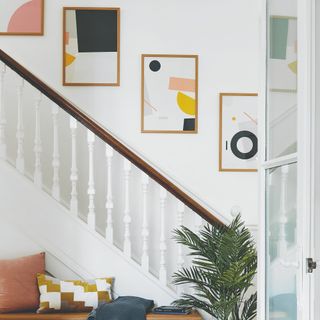 A white hallway with a staircase and a gallery wall of graphic prints